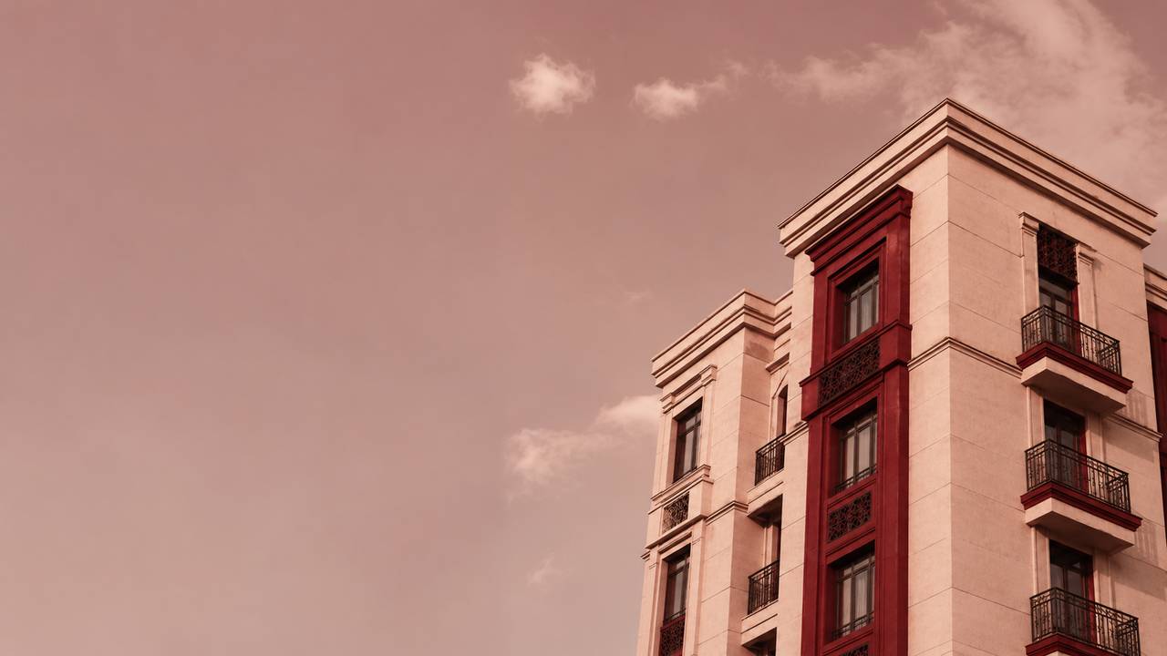 A cream and deep-red apartment building in central Tashkent seen from below against an evening sky.